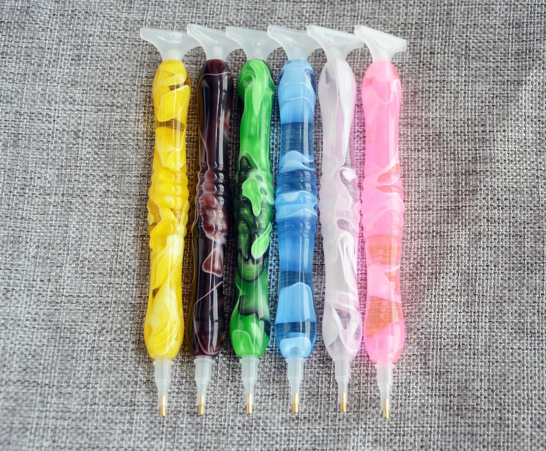 May include: Six diamond painting pens with different colored swirl designs. The pens have a clear plastic handle with a metal tip.
