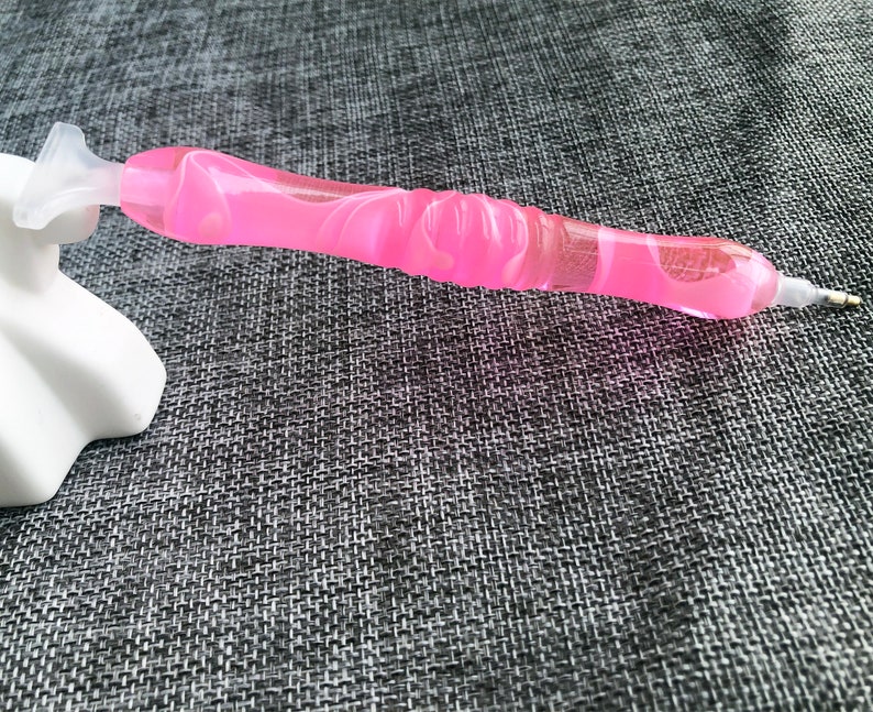 May include: Pink diamond painting pen with a clear plastic tip and a swirl design.