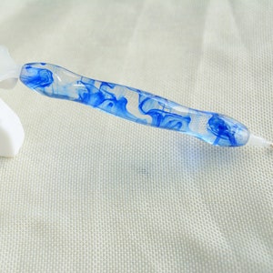 May include: A clear blue and white diamond painting pen with a swirl design. The pen has a gold tip and a white plastic handle.