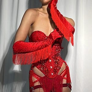 Peut inclure: Un corset rouge avec un bustier et une jupe &agrave; franges. Le corset est orn&eacute; de strass et a un dos &agrave; lacets. Le mod&egrave;le porte des gants rouges &agrave; franges et a un tatouage sur la jambe.