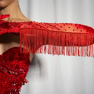 Peut inclure: Gants en satin rouge avec bordure &agrave; franges et strass. Les gants sont port&eacute;s par une personne avec un haut rouge &agrave; paillettes.