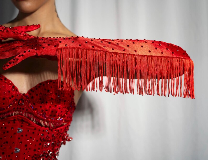 Peut inclure: Gants en satin rouge avec bordure &agrave; franges et strass. Les gants sont port&eacute;s par une personne avec un haut rouge &agrave; paillettes.