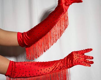 May include: A pair of long red satin gloves with fringe and red rhinestones. The gloves are shown on a person's arms.