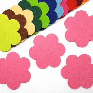 Könnte beinhalten: Eine Auswahl an bunten Filzblüten-Ausschnitten in verschiedenen Farbtönen, darunter Rosa, Grün, Braun und Blau. Mehrere rosa Blüten sind im Vordergrund angeordnet. Diese Bastelmaterialien eignen sich für DIY-Projekte und Dekorationen.