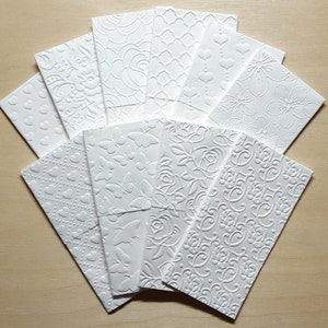 May include: A set of ten white embossed paper envelopes with various patterns, including hearts, flowers, and geometric designs.