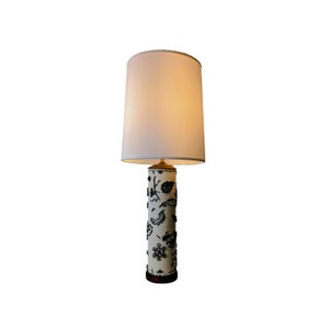 May include: A white lampshade with a black and white patterned base. The lampshade is cylindrical and the base is a cylinder with a floral design.