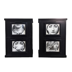 May include: Two black wooden cabinets with three drawers each. Each drawer has a circular image of a woman's face. The top drawer has a woman wearing a necklace, the middle drawer has a woman holding a cup, and the bottom drawer has a woman in a city scene.