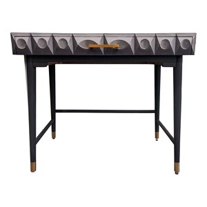 May include: A black desk with a single drawer and gold accents. The drawer front features a geometric pattern in shades of gray.
