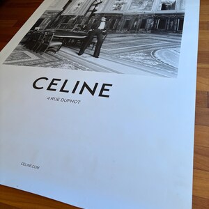 May include: Monochrome poster advertising CELINE, featuring a fashion model in a formal setting. The poster includes the brand name "CELINE", the address "4 RUE DUPHOT", and the website "CELINE.COM". The image is set against a backdrop of a grand interior with a person.