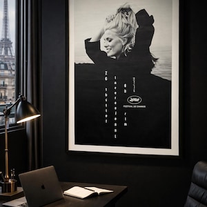 K&ouml;nnte beinhalten: Schwarz-wei&szlig; gerahmtes Poster mit einer blonden Frau und dem Text "Z6 in the event of the 8th Cannes Film Festival". Das Poster h&auml;ngt an einer schwarzen Wand in einem Raum mit Schreibtisch, Laptop und Blick auf den Eiffelturm.