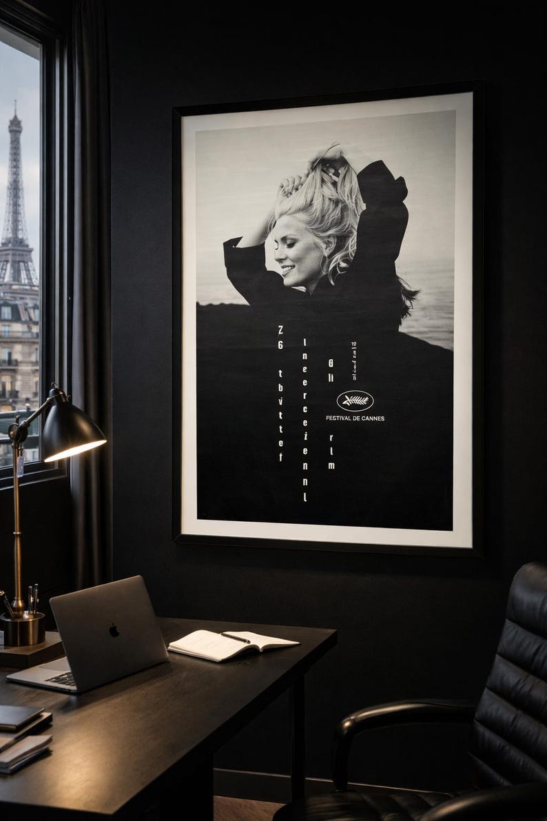 K&ouml;nnte beinhalten: Schwarz-wei&szlig; gerahmtes Poster mit einer blonden Frau und dem Text "Z6 in the event of the 8th Cannes Film Festival". Das Poster h&auml;ngt an einer schwarzen Wand in einem Raum mit Schreibtisch, Laptop und Blick auf den Eiffelturm.