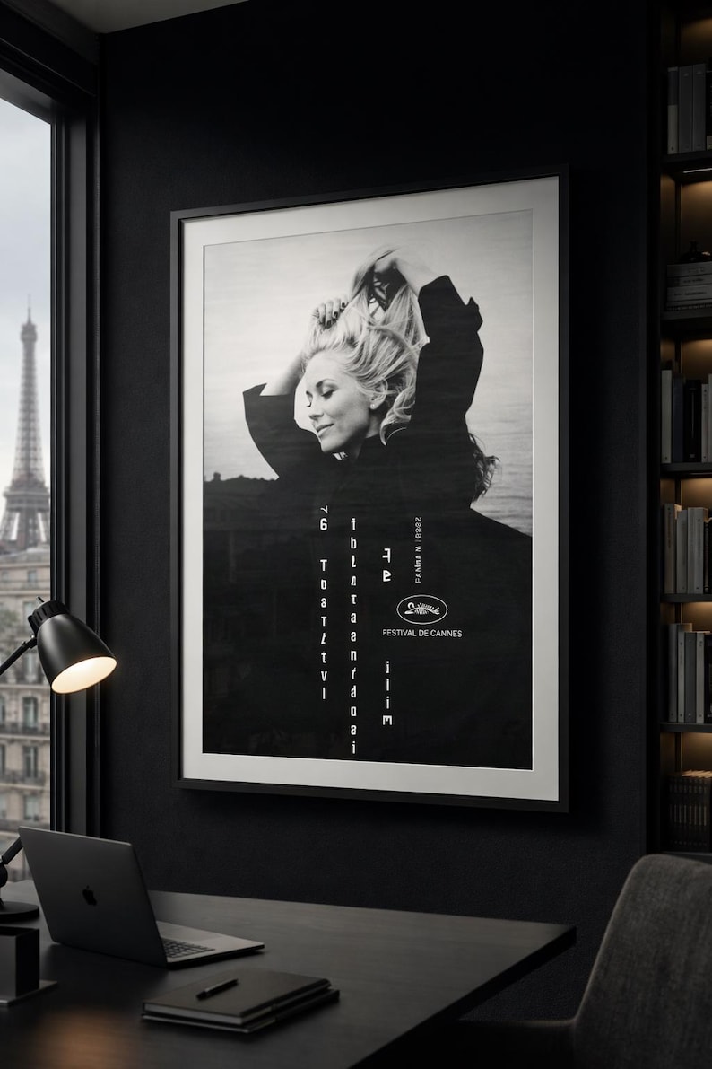 K&ouml;nnte beinhalten: Schwarz-wei&szlig; gerahmtes Poster mit einer Frau mit blonden Haaren, Text und dem Logo des Filmfestivals von Cannes. Das Poster wird in einem dunklen Raum mit einem Schreibtisch, Laptop und Blick auf den Eiffelturm gezeigt.