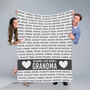 May include: A gray and white sign with the text "Reasons I love being a Grandma" and a heart on each side of the text. The sign is held up by a man and a woman.