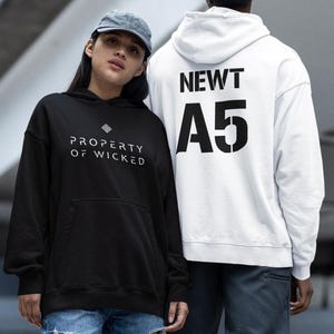 Puede incluir: Dos sudaderas con capucha, una negra con el texto "PROPERTY OF WICKED" y la otra blanca con el texto "NEWT A5".