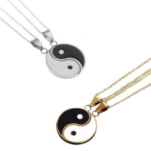 May include: Two matching necklaces featuring yin and yang pendants. One pendant is silver-toned with a black and white design, the other gold-toned. Both necklaces have delicate chains.