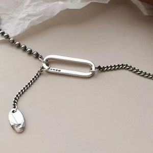 Peut inclure: Un collier en argent au design unique. Il se compose d'une chaîne de petites perles, d'un grand maillon ovale et d'une chaîne avec un petit pendentif ovale. Le pendentif porte l'inscription "S925".