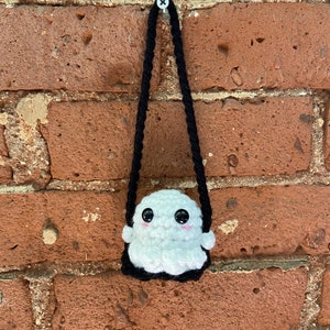 May include: A white crocheted ghost with black eyes and a black mouth hanging from a black string on a brick wall.