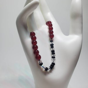 May include: A red and black beaded bracelet with a black cord. The bracelet has alternating red and black beads.