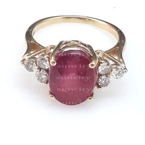 May include: A gold ring featuring a large oval ruby gemstone and smaller diamond accents.