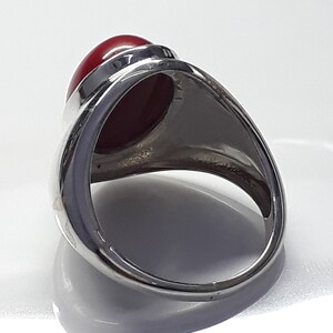 May include: A silver ring with a large, oval-shaped, red gemstone set in the center. The ring is designed with a raised bezel setting.