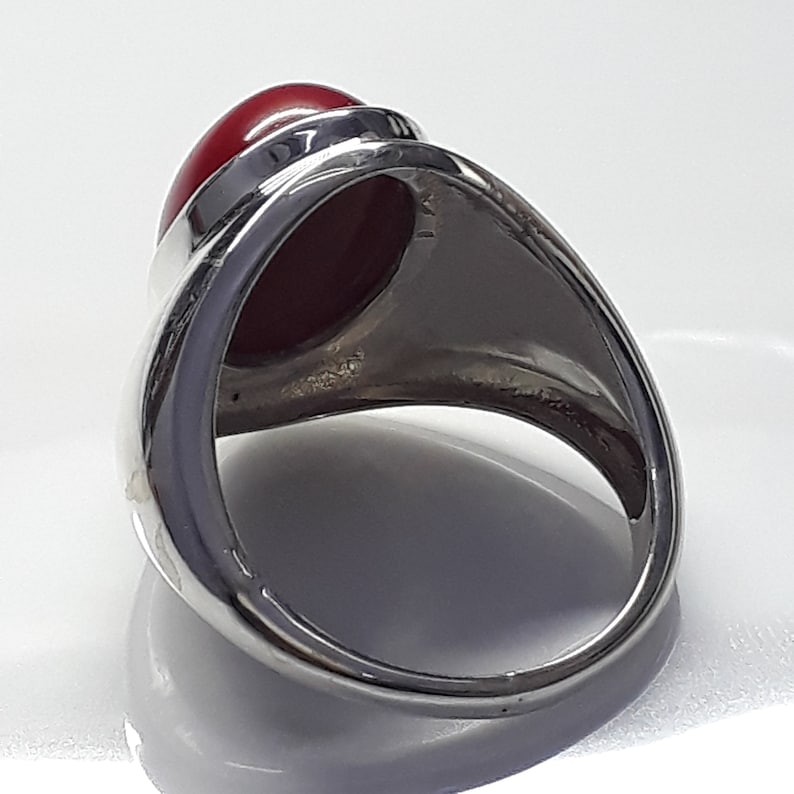 May include: A silver ring with a large, oval-shaped, red gemstone set in the center. The ring is designed with a raised bezel setting.