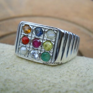 May include: A silver ring with a square face featuring nine colorful gemstones. The ring has a ribbed design on the sides and the text "SUNCITYJEWELS" is visible. The gemstones are in various colors, including red, blue, and green.