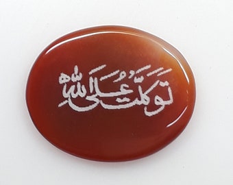 May include: A red carnelian stone with the Arabic phrase "La ilaha illa Allah" engraved in white.