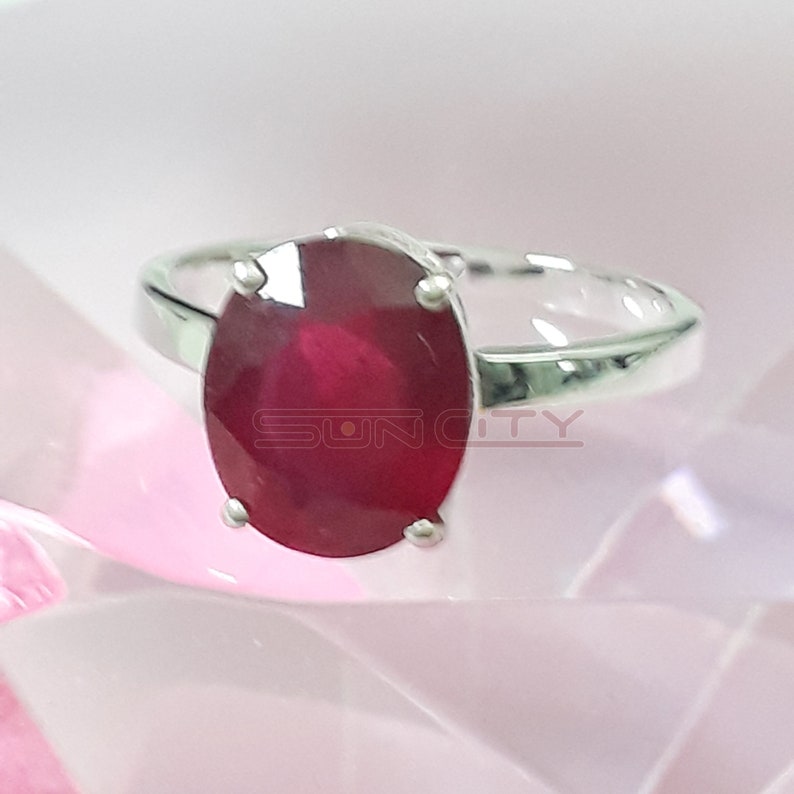 May include: A silver ring featuring a large, oval-shaped ruby gemstone. The ruby is a deep red colour and is set in a simple, elegant setting.