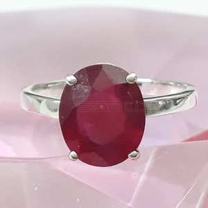 May include: A silver ring with a large, oval-shaped ruby gemstone. The ruby is a deep red color and has a faceted cut.