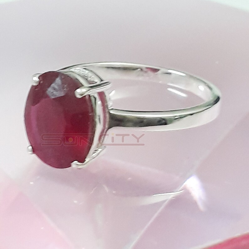 May include: A silver ring featuring a large, oval-shaped, red gemstone.