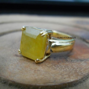Può includere: Un anello d'oro con una grande pietra preziosa gialla a taglio quadrato. L'anello ha una semplice fascia in oro lucido e un'incastonatura a quattro griffe. Il testo "SUNCITYJEWELS" è visibile sull'anello.