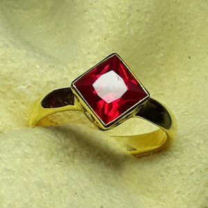 Op de afbeelding: Een gouden ring met een vierkante rode edelsteen.