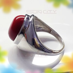 May include: A silver ring with a large, round, red gemstone. The ring has a wide band with a smooth, polished finish.