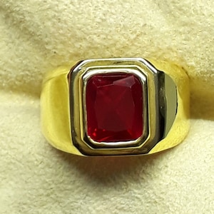 May include: A gold ring with a large, red, square-shaped gemstone.
