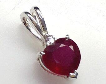 May include: A silver pendant featuring a heart-shaped ruby gemstone with a small clear stone accent.
