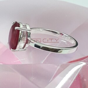 May include: A silver ring featuring a large, oval-shaped ruby gemstone. The ring is set in a simple, elegant design.