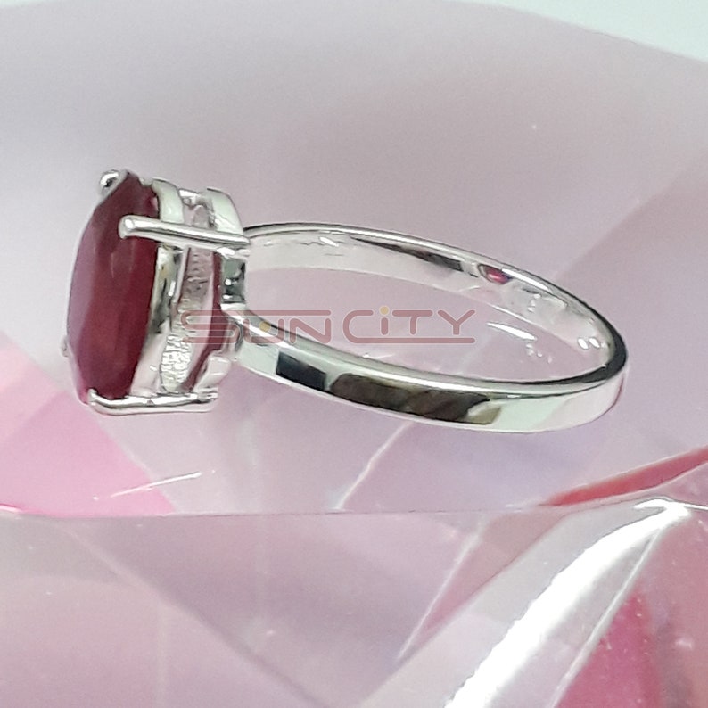 May include: A silver ring featuring a large, oval-shaped ruby gemstone. The ring is set in a simple, elegant design.