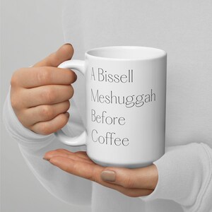 May include: White ceramic coffee mug with black text that reads "A Bissell Meshugah Before Coffee".