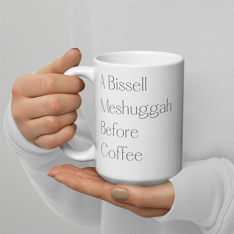 May include: White ceramic coffee mug with black text that reads "A Bissell Meshugah Before Coffee".