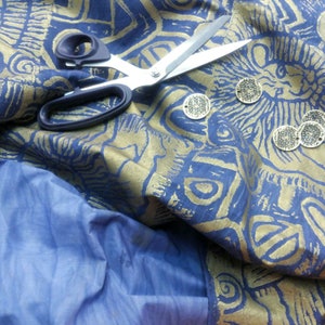 May include: A blue fabric with gold metallic designs and a pair of silver scissors. There are several gold metal circular embellishments on the fabric.