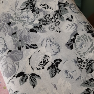 Puede incluir: Una tela blanca con un patr&oacute;n floral con rosas y hojas negras y grises.