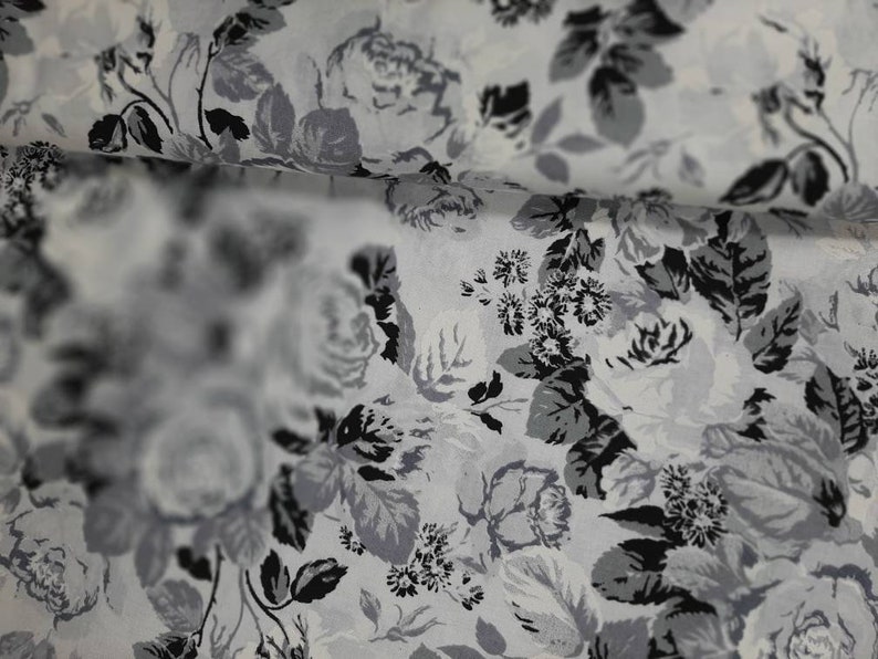 Puede incluir: Una tela blanca con un patr&oacute;n floral negro y gris. La tela tiene un brillo sutil y una textura suave.