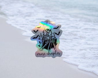 May include: A holographic sticker with a skeleton reading a book. The sticker has bats and vines around the skeleton and the text "Just one more chapter".