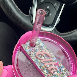 Puede incluir: Un vaso rosa con tapa rosa y una pajita. La tapa tiene una etiqueta de nombre rosa brillante que dice "Ellie".
