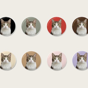 Könnte beinhalten: Acht runde Buttons mit einem Porträt einer getigerten Katze und dem Namen "kiri" in Schreibschrift. Jeder Button hat einen anderen farbigen Hintergrund: Schwarz, Grün, Rot, Braun, Beige, Hellbraun, Rosa und Lila.