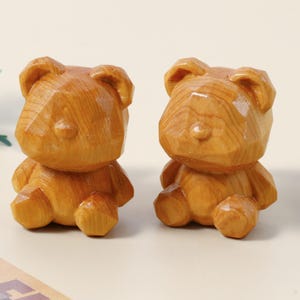 Könnte beinhalten: Zwei Holz-Bärenfiguren mit geometrischem Design. Die Bären sind aus hellbraunem Holz geschnitzt und haben eine glänzende Oberfläche. Sie sitzen nebeneinander auf einer hellen Oberfläche. Die Bären sind ein dekorativer Artikel.