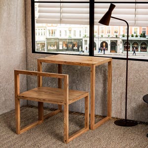 Puede incluir: Un conjunto de mesa y silla de madera con un diseño simple y moderno. La mesa tiene una tapa rectangular y una base cuadrada. La silla tiene un asiento rectangular y un respaldo con una sola barra horizontal. El conjunto está hecho de madera natural con un acabado marrón claro.