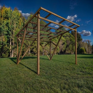 Puede incluir: Una estructura de madera con un techo de listones y una cubierta de plástico transparente. La estructura está de pie en un campo de hierba con árboles en el fondo.