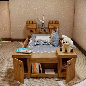 May include: A wooden castle-themed bed frame with storage compartments and a grey and white polka dot duvet. The bed is decorated with a stuffed bunny and a stuffed dog.