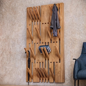 Puede incluir: Un perchero de pared de madera con múltiples estantes y ganchos inclinados. El perchero está hecho de madera natural y tiene un aspecto rústico. Una chaqueta, un paraguas y libros se muestran en el perchero.